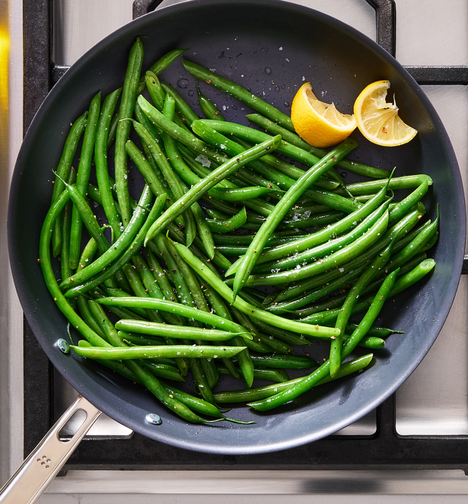 Sautéed green beans with lemon wedges and seasoning in a nonstick skillet